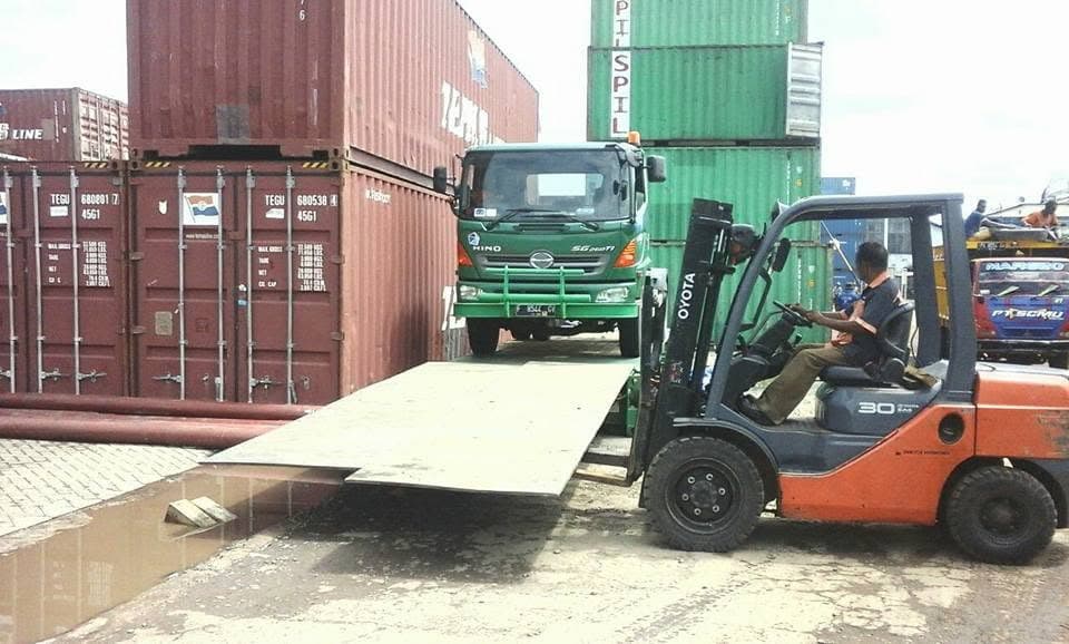Forklift membantu proses pemuatan di antara truk dan deretan kontainer